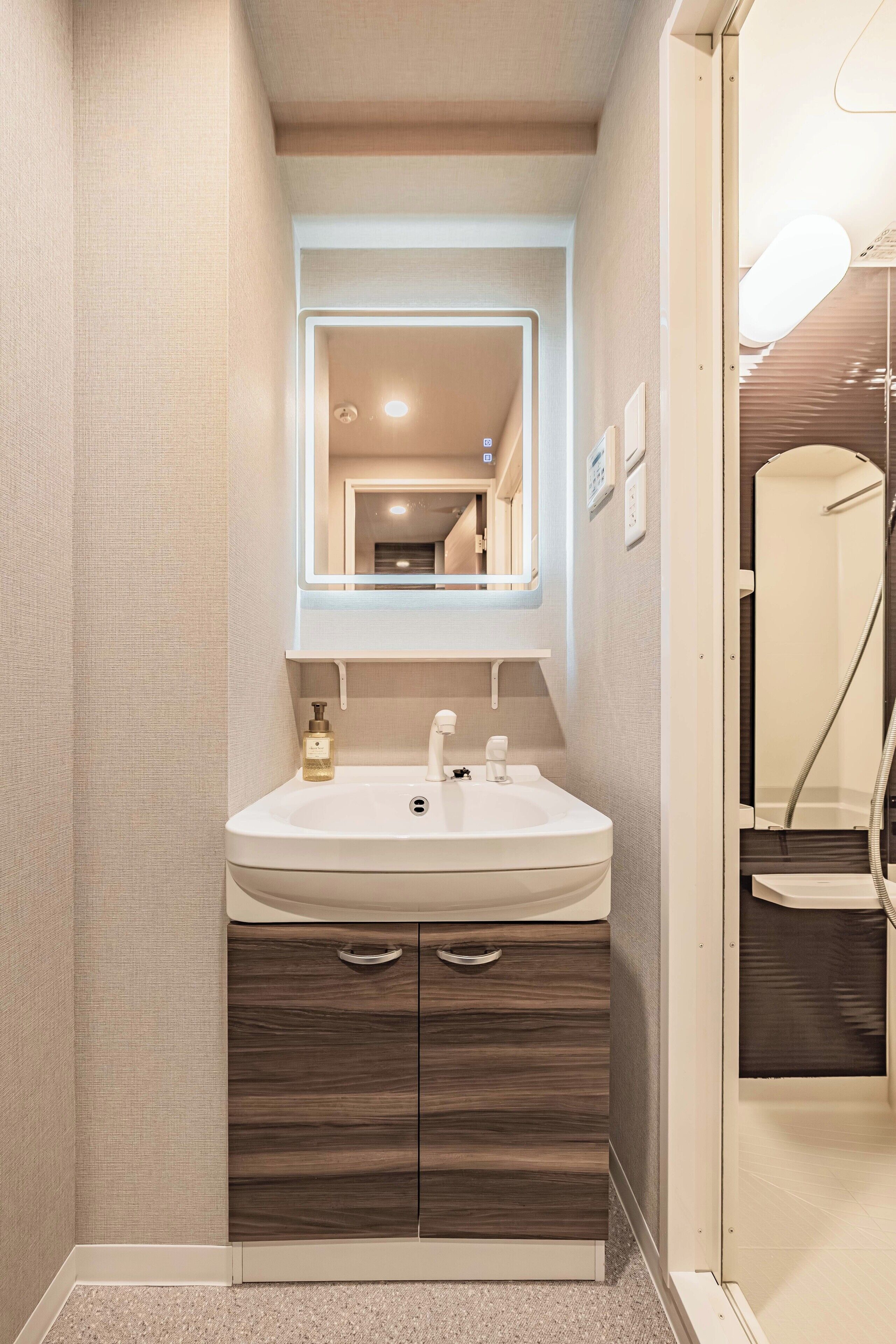 A bathroom with a white sink, wooden vanity, a mirror, and a shower area.