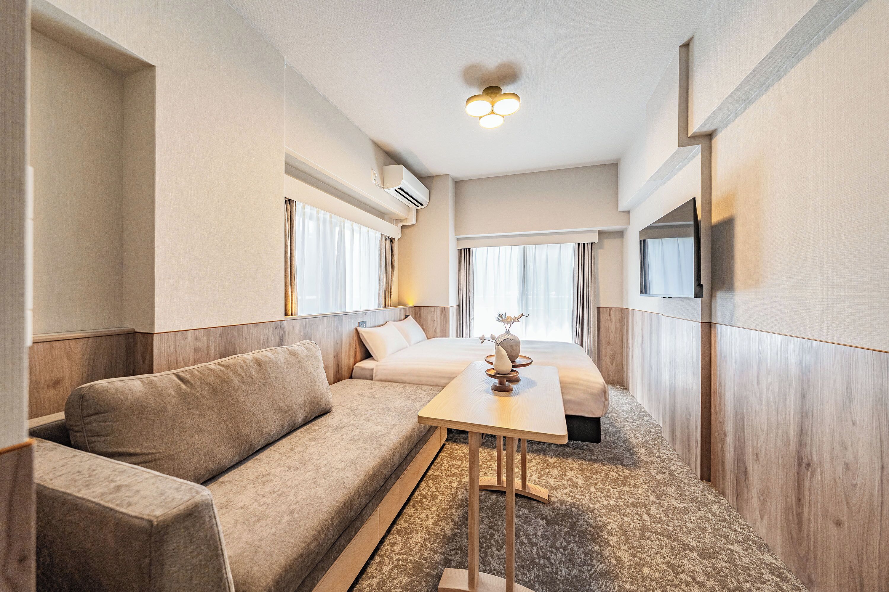 A hotel room with a sofa, a small table with a vase, and a bed.