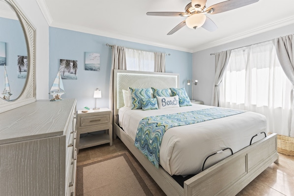 Ein Schlafzimmer mit Bett, Nachttischen, Kommode, Deckenventilator und Kunstwerken an den Wänden.