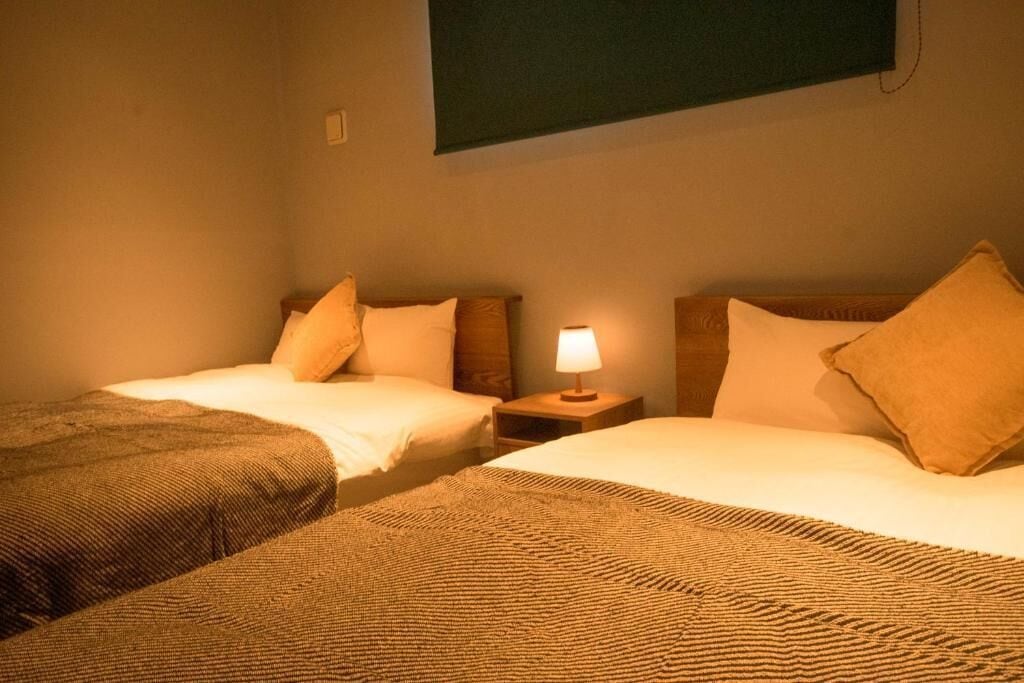 Een hotelkamer met twee enkele bedden, een nachtkastje met een lamp en een aan de muur bevestigde televisie.