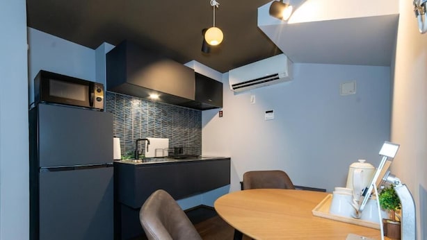 A modern kitchen with a built-in microwave, refrigerator, and a small dining area with a table and chairs. - Nadeshiko Machiya (Fukuoka City Hakataku  Katakasu)
