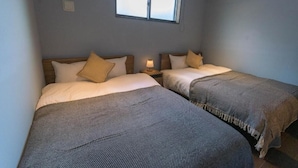 A room with two beds, each with a headboard, a bedside table with a lamp, and a window above the beds. - Nadeshiko Machiya (Fukuoka City Hakataku  Katakasu)