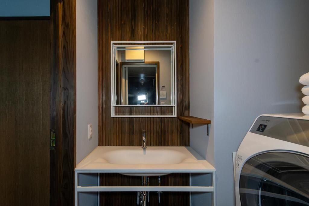 A bathroom with a wooden vanity, a mirror, a sink, and a washing machine.