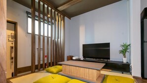 A modern living room with a flat-screen TV, a low wooden coffee table, and yellow cushions. - Nadeshiko Machiya (Fukuoka City Hakataku  Katakasu)