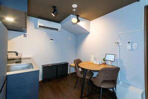 A compact kitchen with a sink, a small refrigerator, and a dining area with a table and chairs. - Nadeshiko Machiya (Fukuoka City Hakataku  Katakasu)