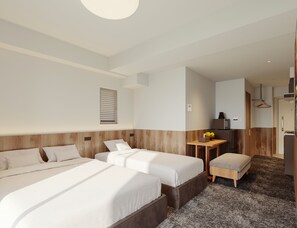 Ett hotellrum med två sängar, ett litet bord med en fruktskål och en liten köksdel.