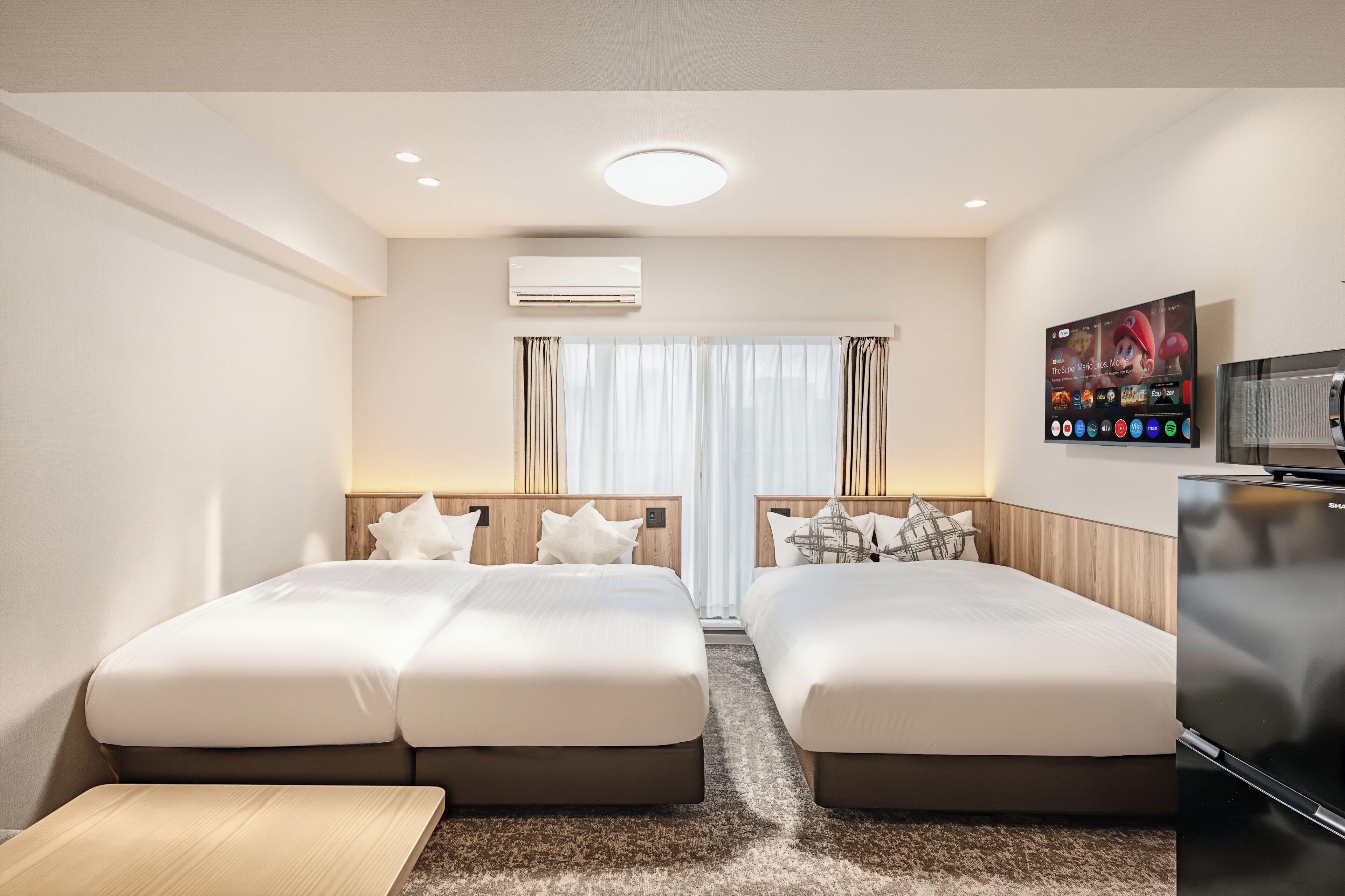 A hotel room with two beds, a TV, an air conditioner, and a flat-screen TV mounted on the wall.
