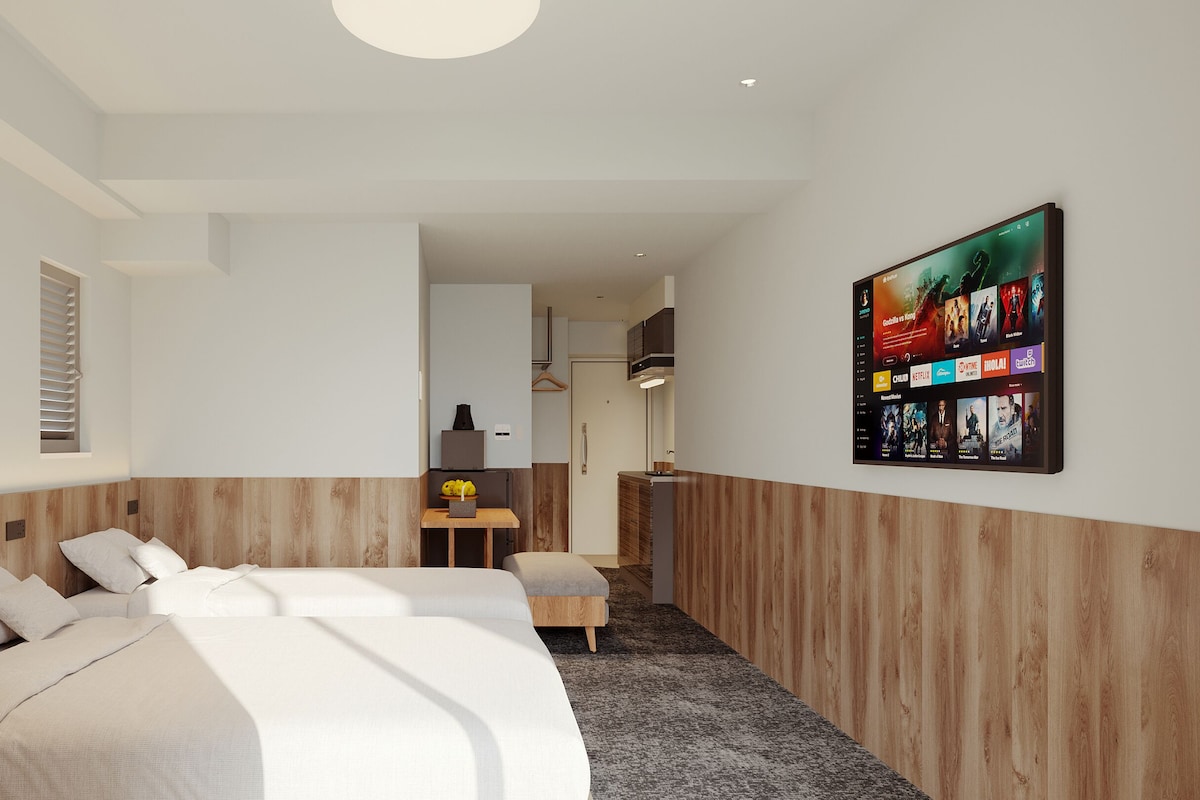 A modern hotel room with a large bed, a small table, and a wall-mounted TV displaying a movie selection.