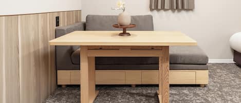 A small, modern room with a wooden table, grey sofa, and a grey carpet.