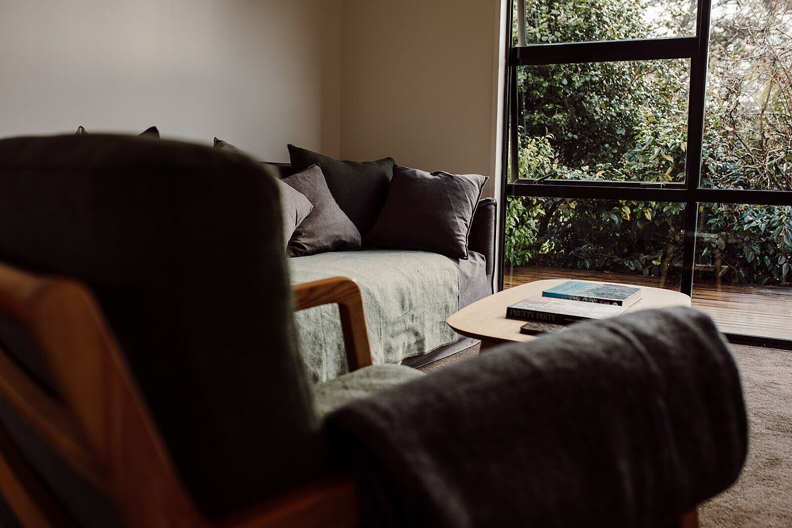 A room with a sofa, a coffee table, and a view of greenery through a window.