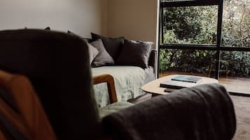 A room with a sofa, a coffee table, and a view of greenery through a window.