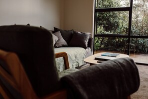 Ein Zimmer mit einer Couch, einem Couchtisch und Blick auf Grün durch ein Fenster.