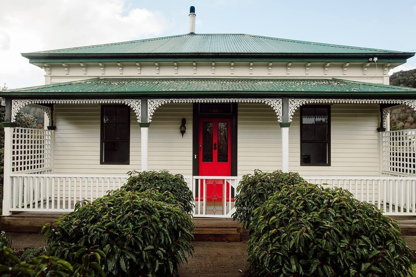 A two-story building with a green roof, white siding, and a red front door.