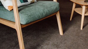 A green armchair with a cushion, a floor lamp, a small round table, and a potted plant in a living room.