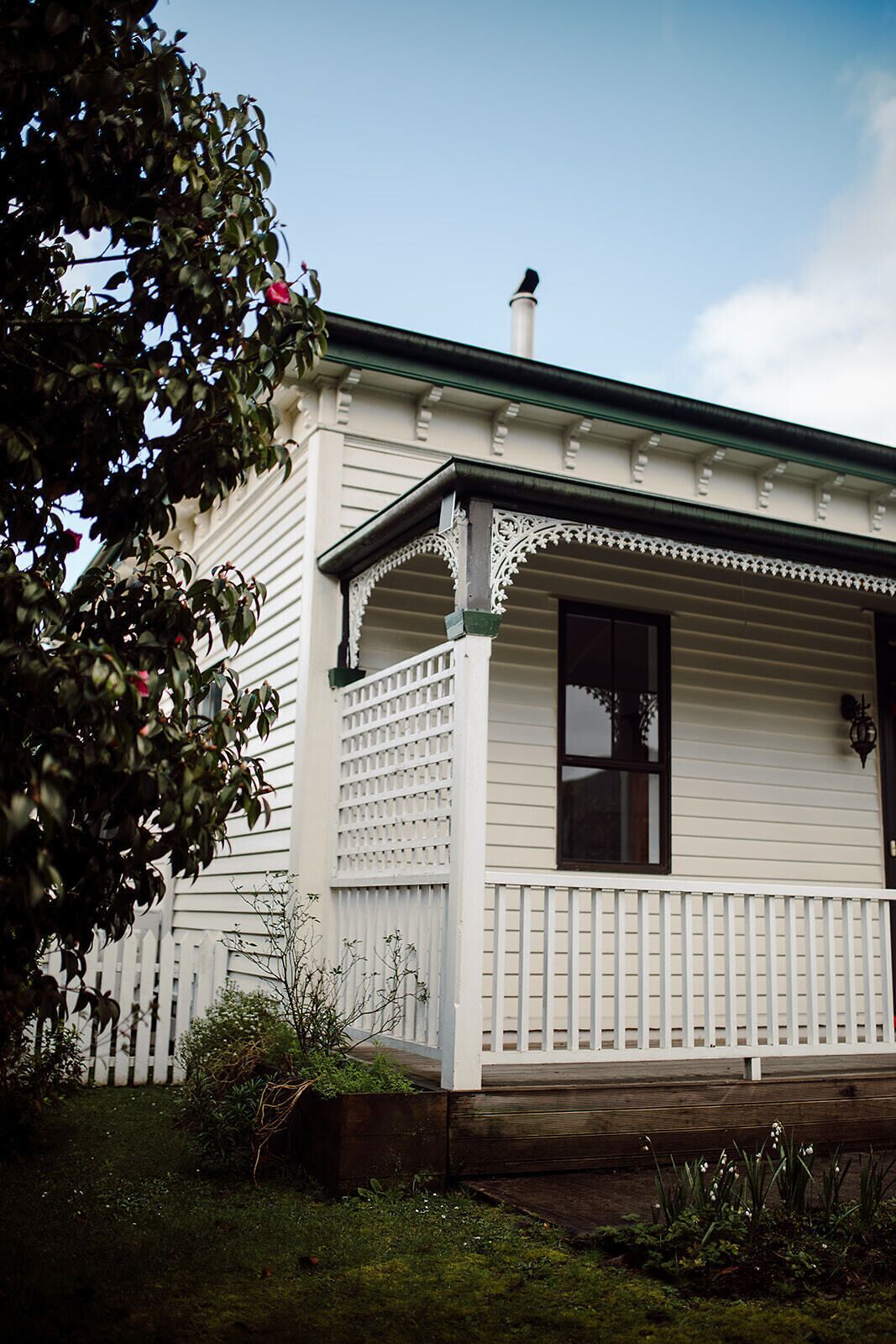 A white house with a porch, a chimney, and a white picket fence.