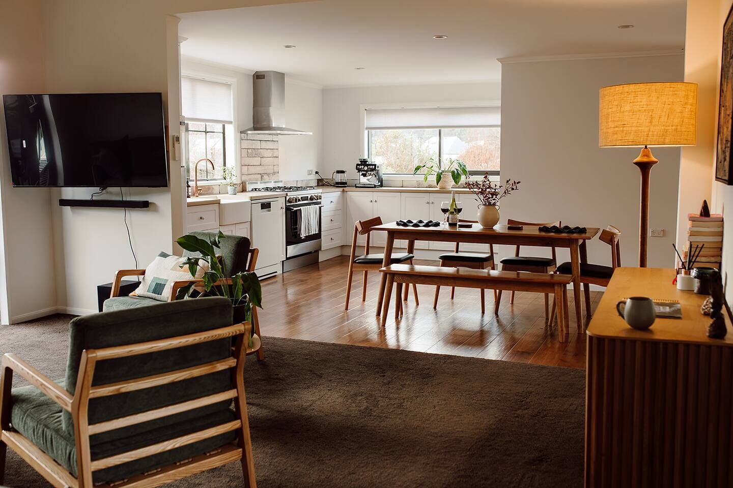 A modern kitchen with a dining area, a flat-screen TV mounted on the wall, and a large window providing natural light.