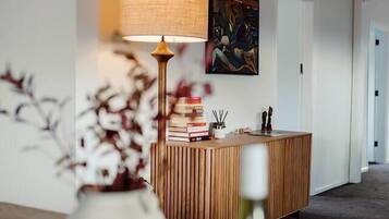 A modern living room with a wooden reception desk, a lamp, a vase with flowers, and a painting on the wall.
