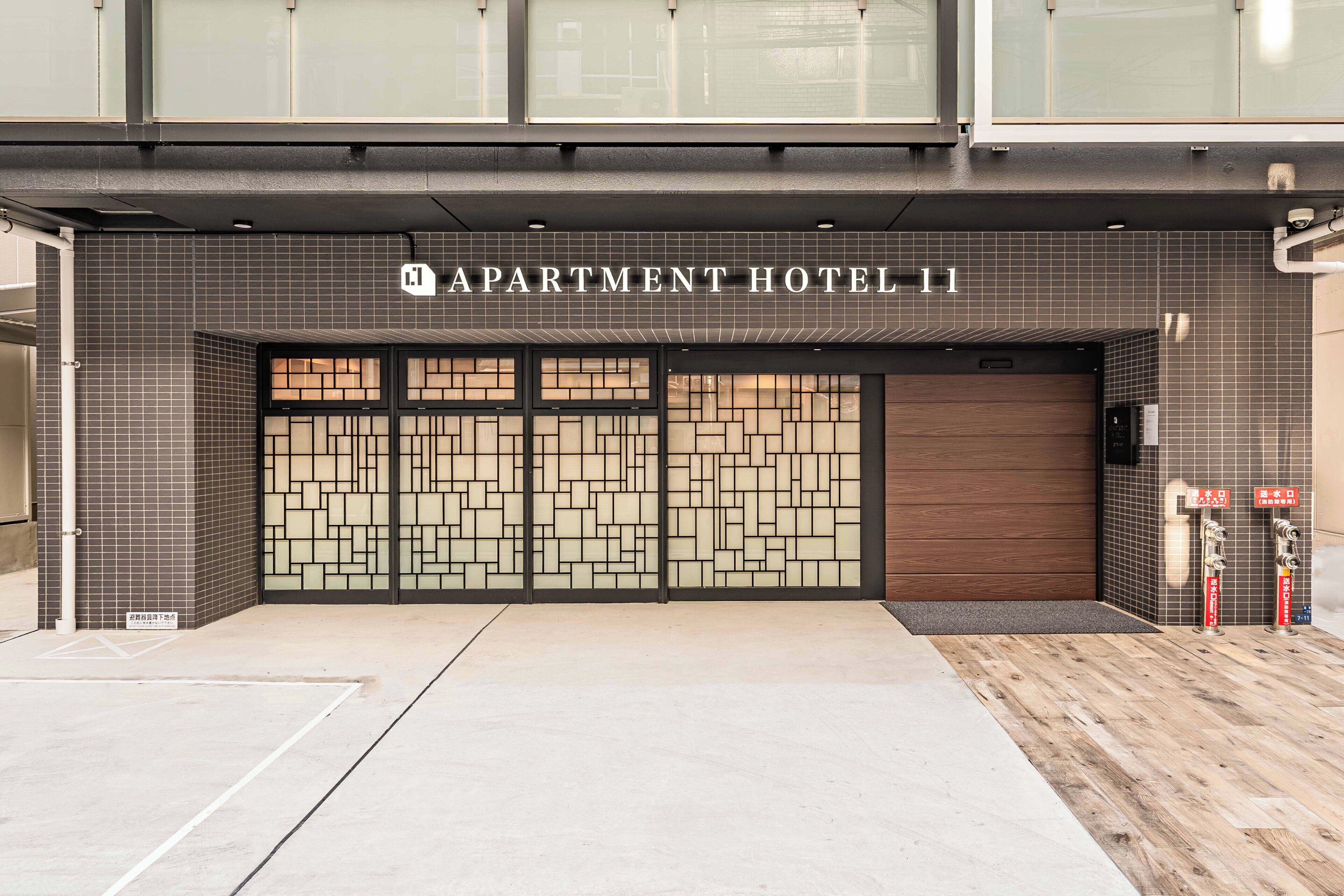 The entrance to Apartment Hotel 11 with a tiled facade, a large wooden door, and a small entrance area with a mat.