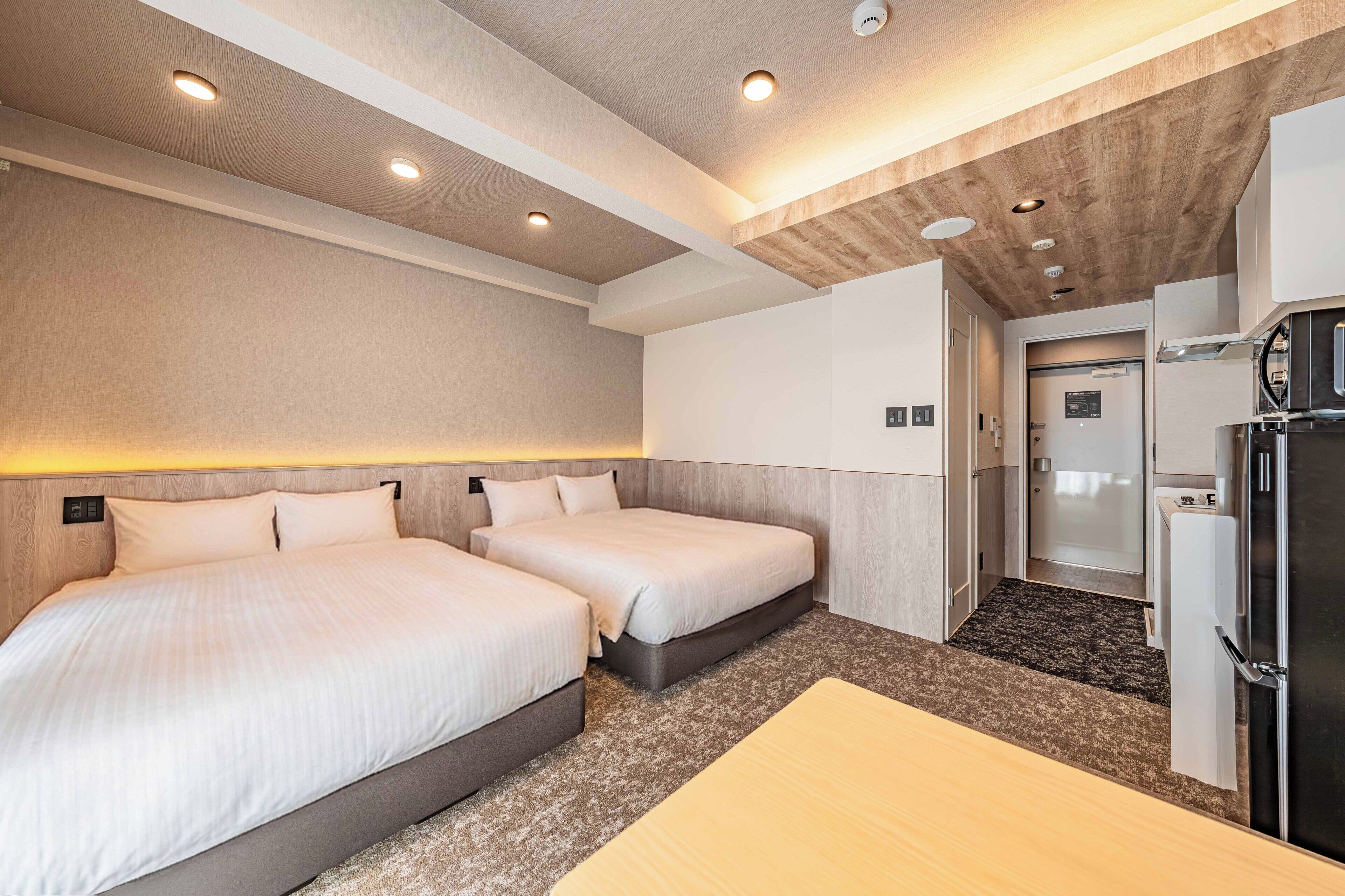 Habitación de hotel con dos camas, una kitchenette y un baño.