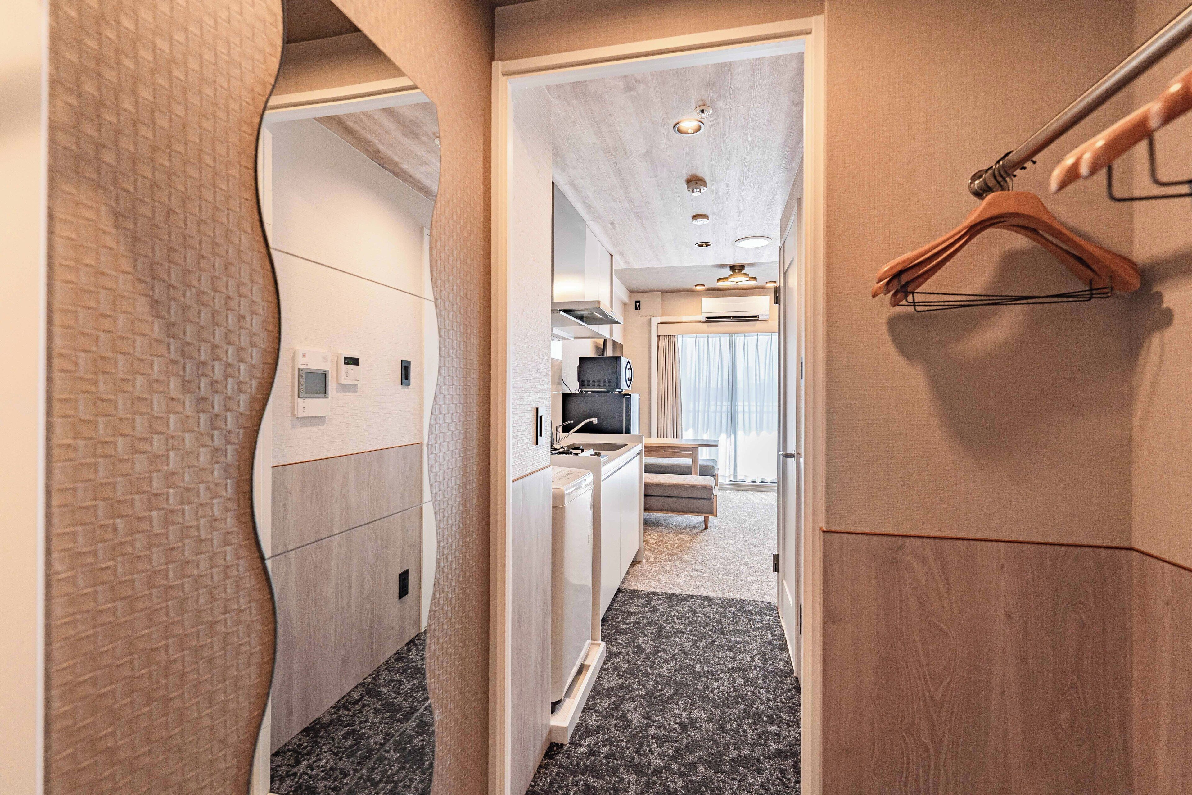 A narrow hallway with a kitchen area, a hanging coat rack, and a bathroom with a shower.