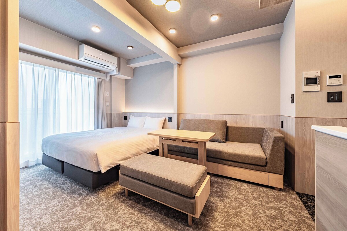 A modern hotel room with a bed, a sofa, a small table, and a desk.
