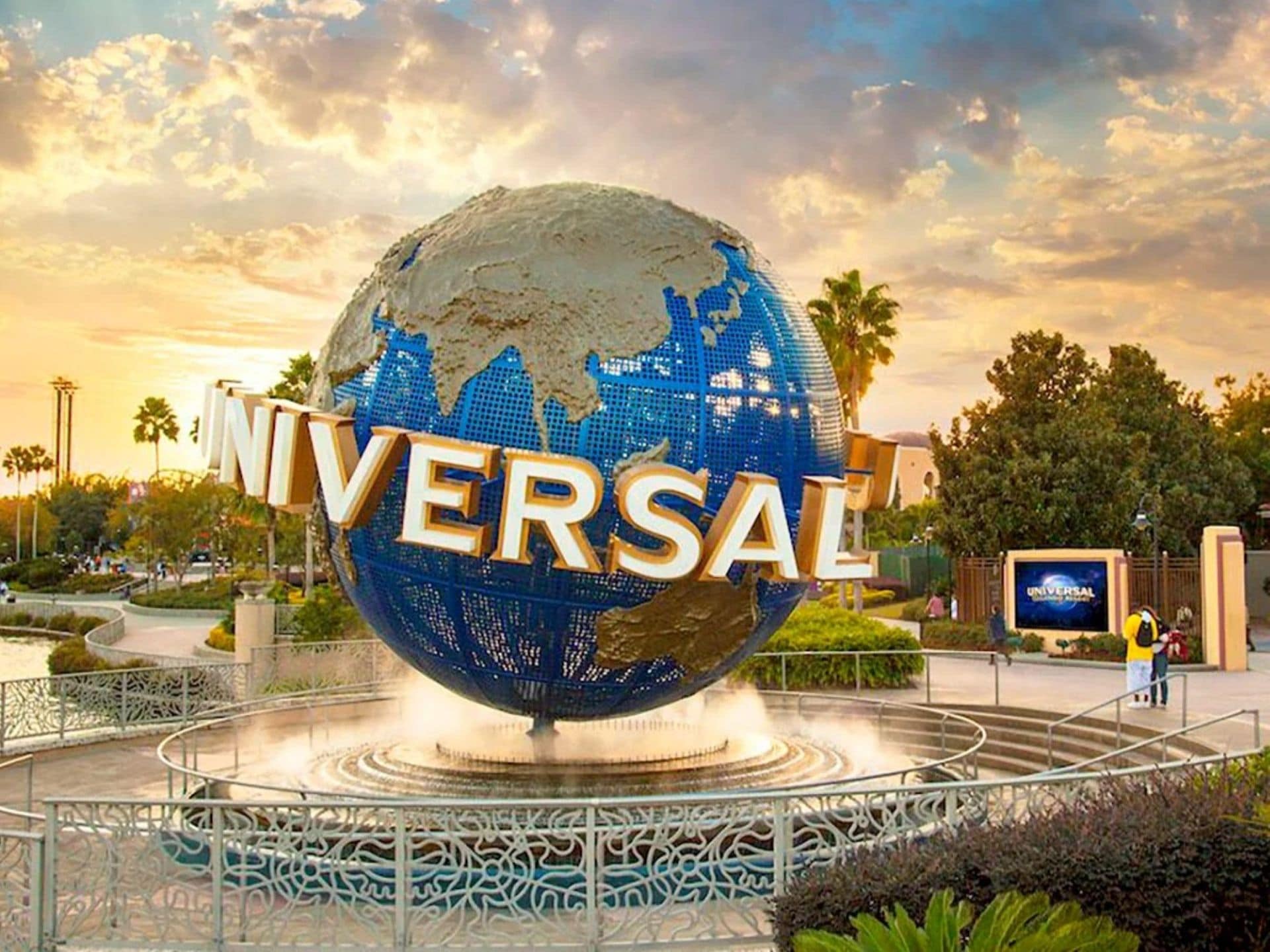 En klode med ordet 'UNIVERSAL' påtrykt, omgivet af et dekorativt hegn og palmer.