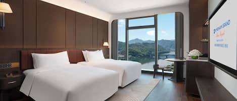 Habitación de hotel con dos camas, un ventanal con vistas a la montaña, una mesita con un florero y un televisor montado en la pared.