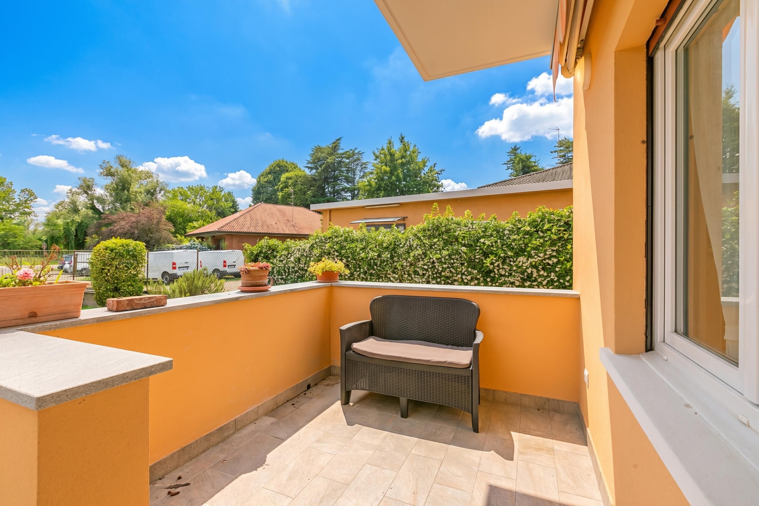 A balcony with a chair, potted plants, and a view of the surrounding area.