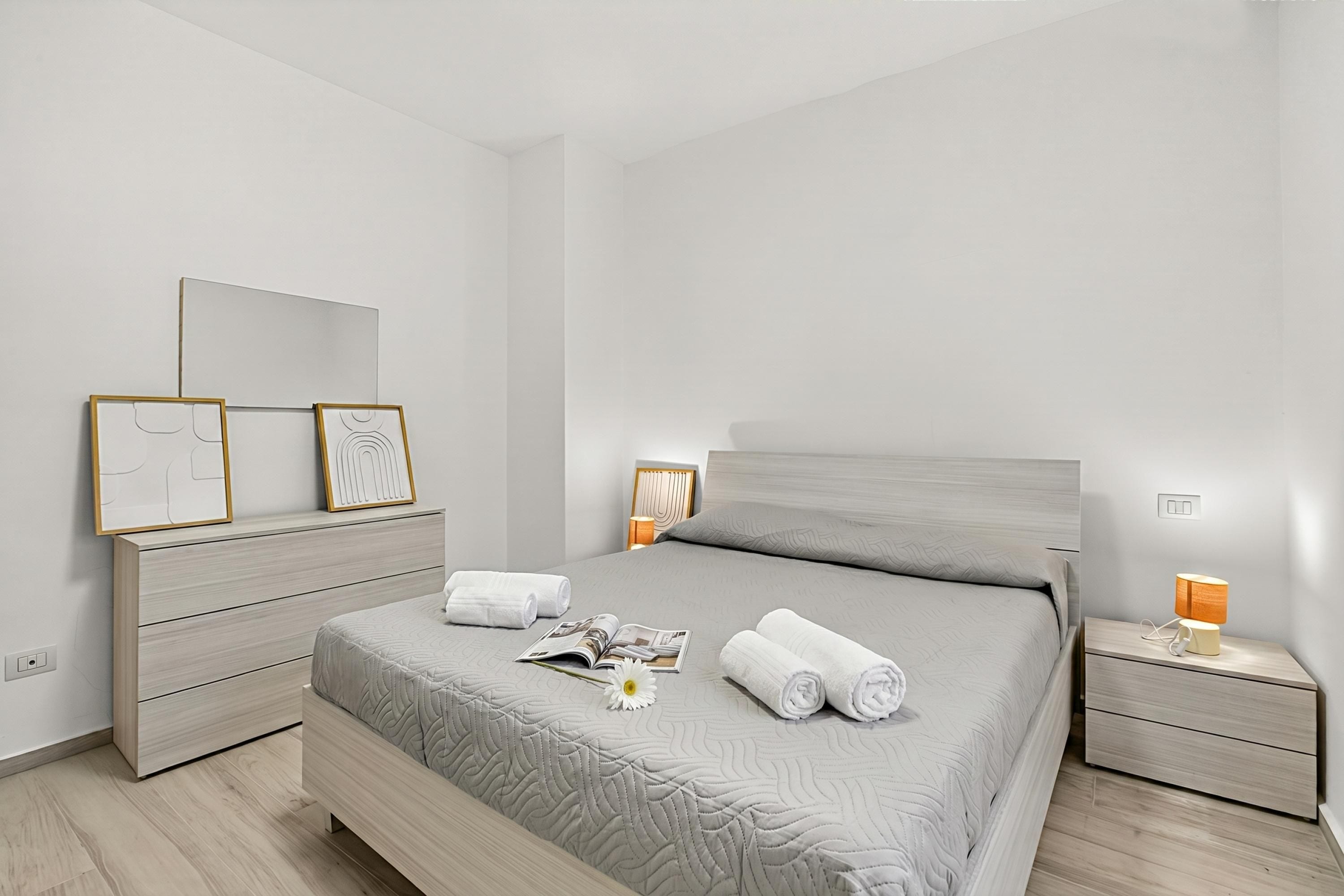 Un dormitorio moderno con cama, mesitas de noche, cómoda y cuadros en la pared.