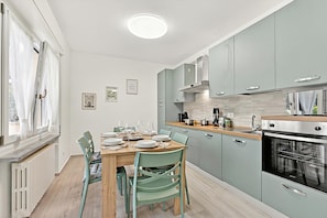 Eine moderne Küche mit hellblauen Schränken, einem Holzes Esstisch und einem eingebauten Backofen.