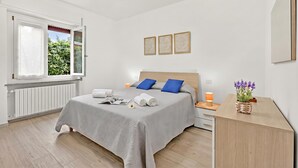 A modern bedroom with a bed, bedside tables, a desk, a window, and a view of greenery. - Diamond Lake Apartment 13918 (Angera)