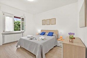 Ein modernes Schlafzimmer mit Bett, Nachttischen, einem Schreibtisch, einem Fenster und Blick auf Grünflächen.