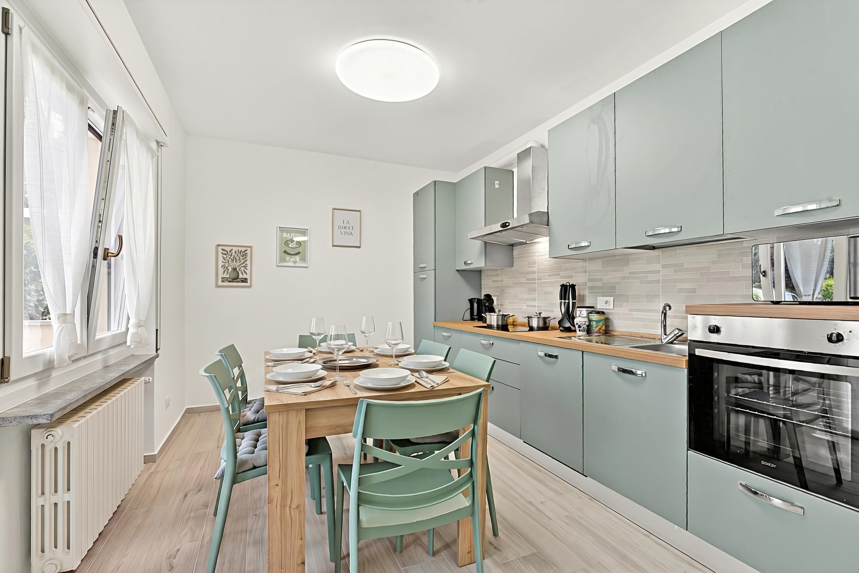 A modern kitchen with light blue cabinets, a wooden dining table, and a built-in oven.