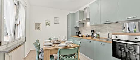 A modern kitchen with light blue cabinets, a wooden dining table, and a built-in oven.