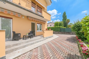 Ein zweistöckiges Gebäude mit einem Balkon, Sitzgelegenheiten im Freien und einem Ziegelweg, der zum Eingang führt.