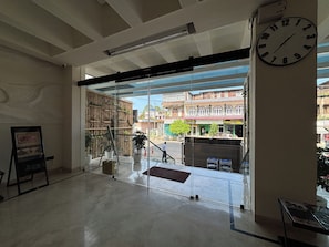 Un espacio interior con un amplio ventanal, un reloj y vista a la calle.