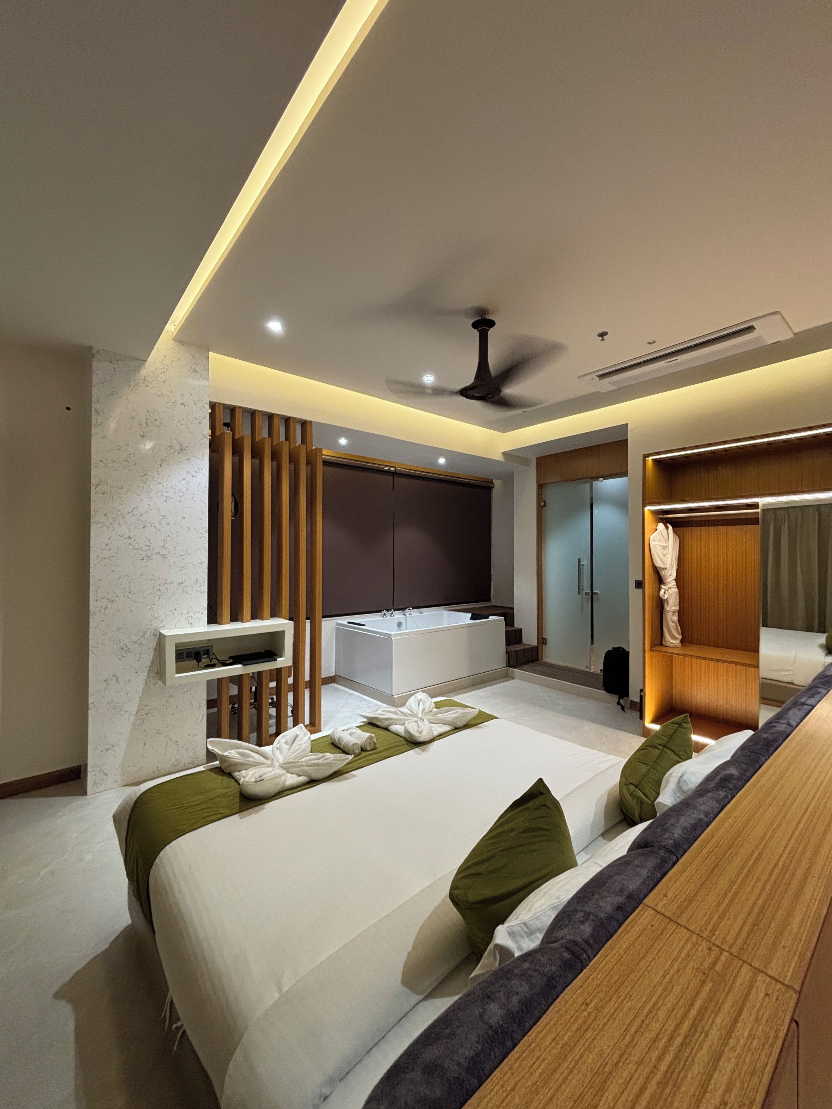 A modern hotel room with a bed, a sitting area, a bathtub, and a wardrobe.