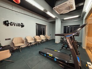 Un gimnasio con equipo de ejercicio, incluyendo una cinta de correr y bicicletas estáticas, y varias sillas.