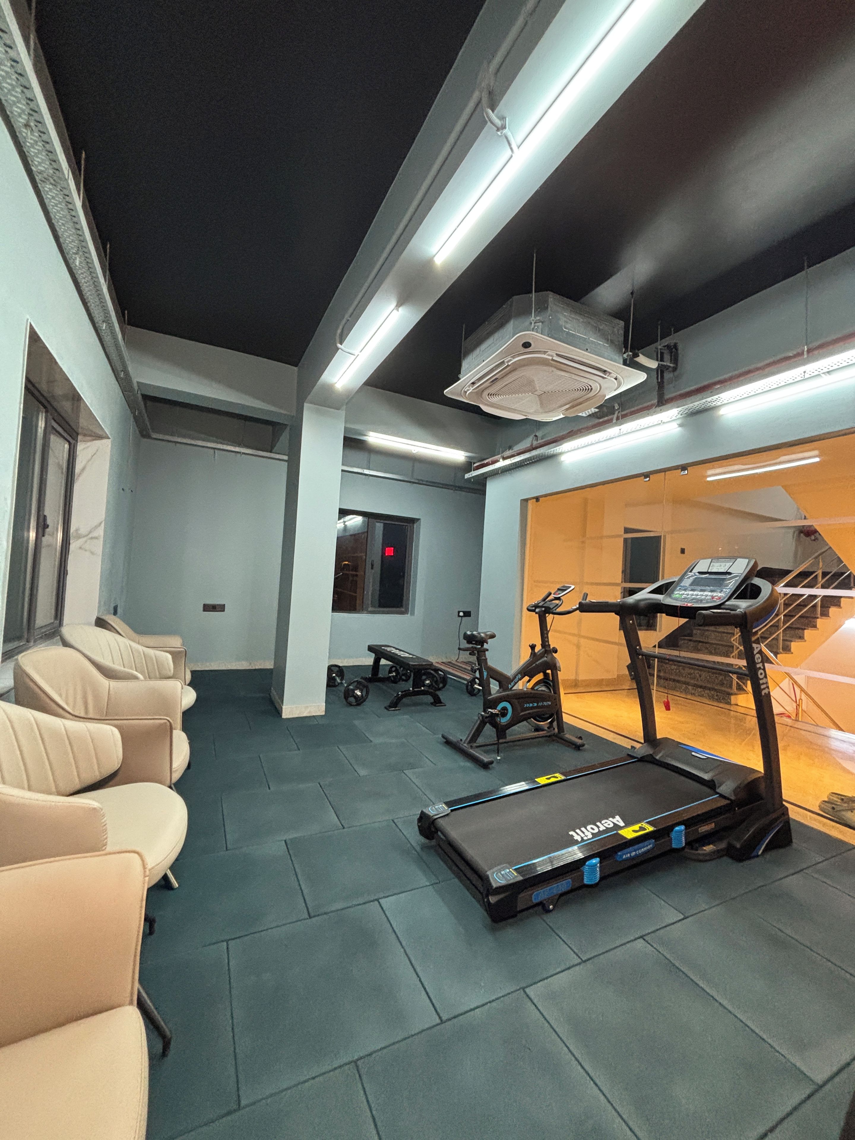 Une salle de sport équipée de matériel d’exercice, d’un tapis de course et d’un ventilateur fixé au mur.