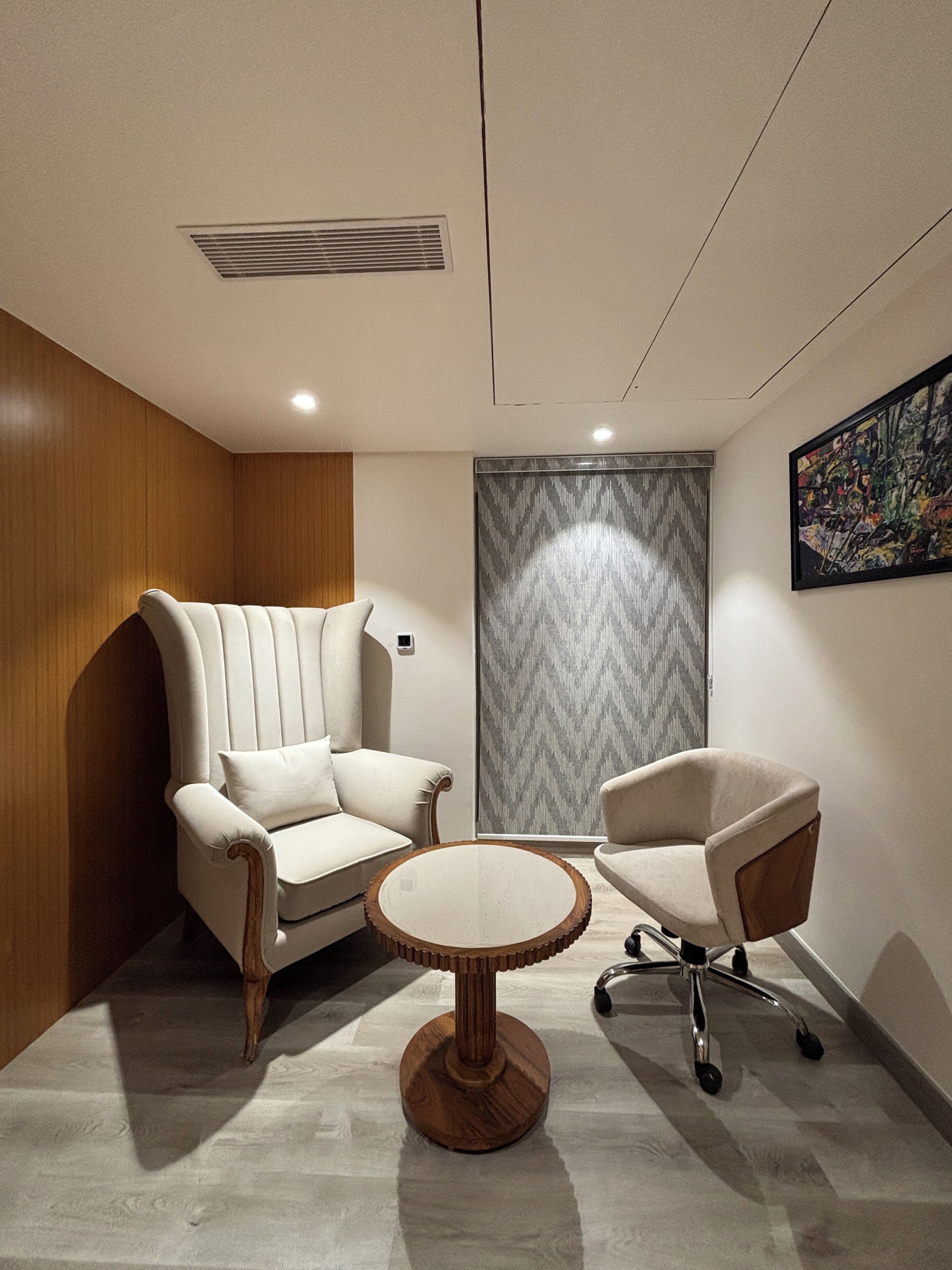 Una habitación moderna con un revestimiento de madera, un sillón grande, una silla más pequeña y una mesa redonda.