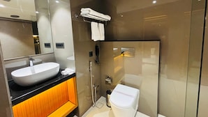 Et moderne badeværelse med et stort spejl, en hvid vask, et toilet og et bruseområde med glasvægge.