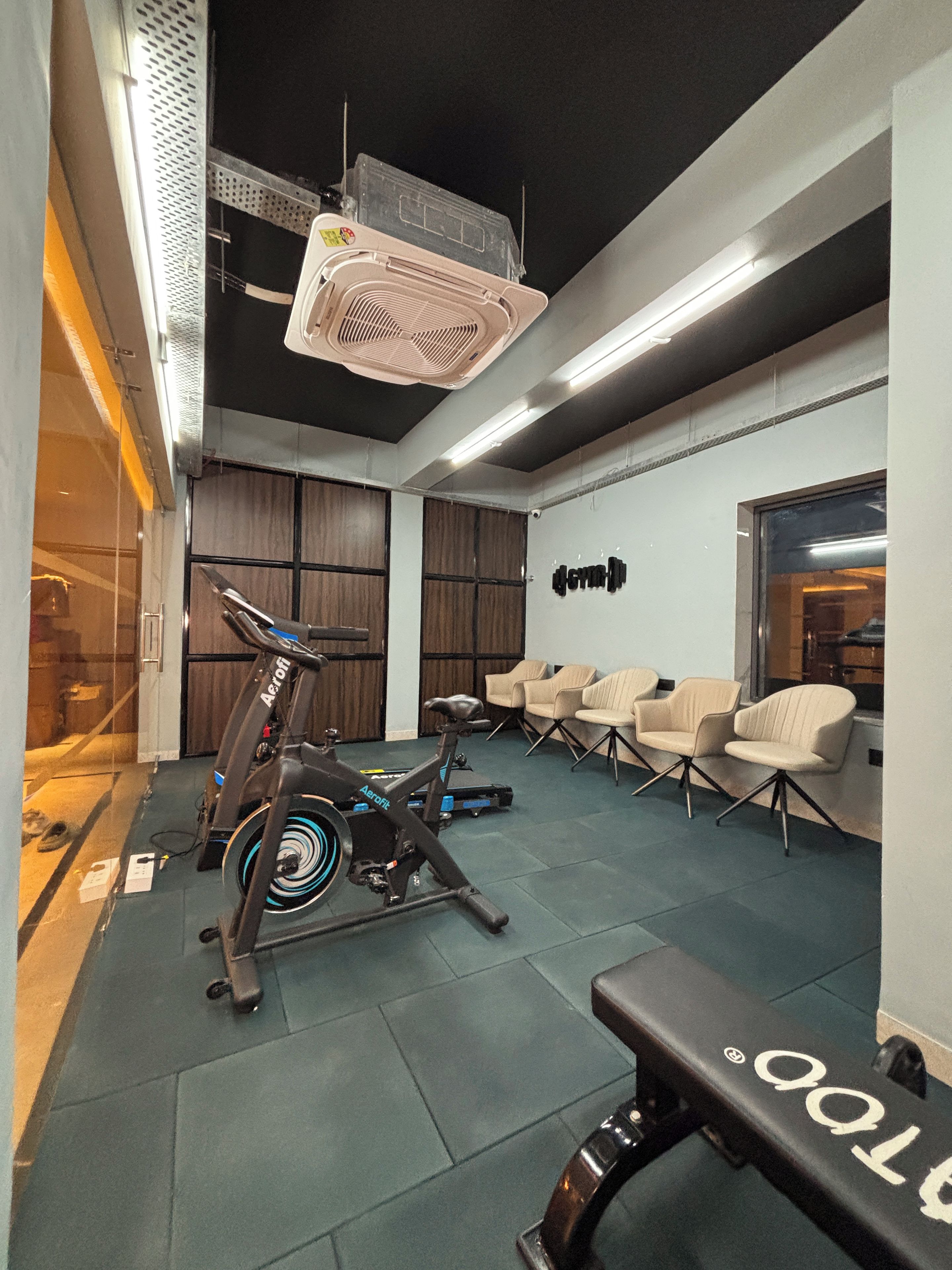 Un gimnasio moderno con equipamiento de ejercicio, zonas de descanso y un banco.