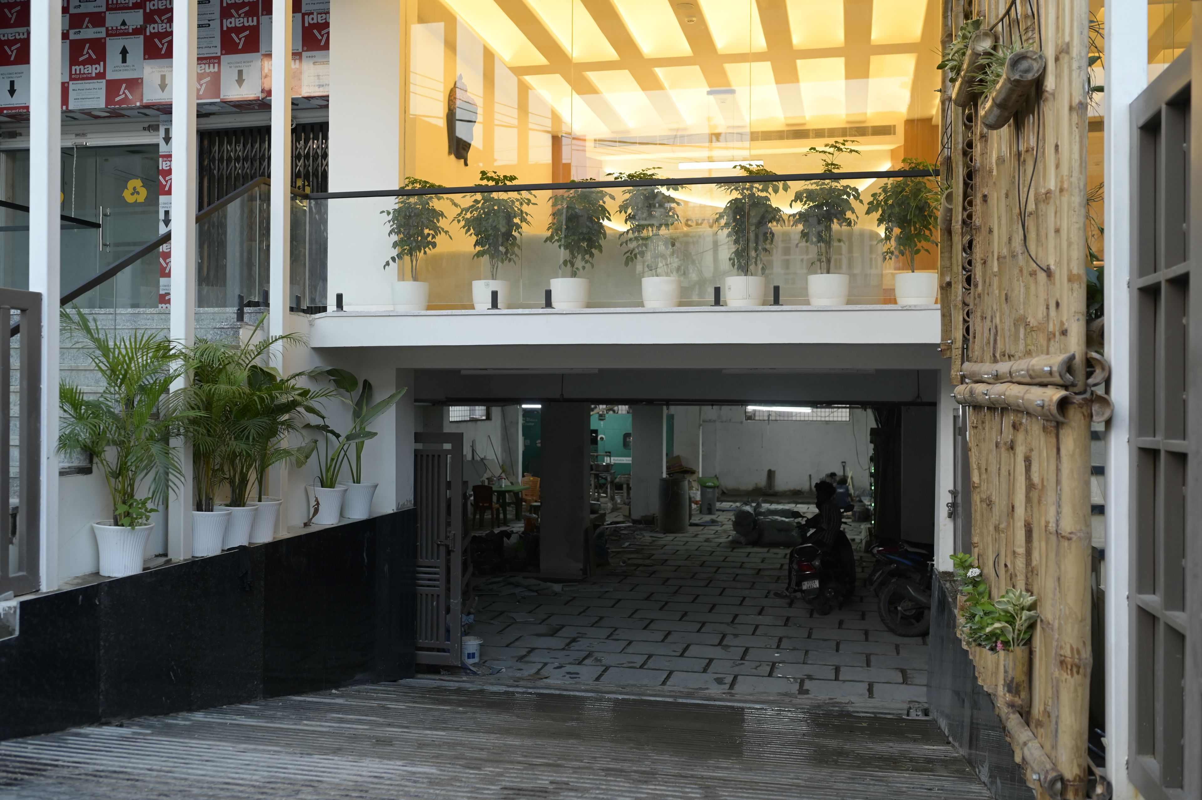 Entrada de un edificio con una marquesina, plantas en macetas y una motocicleta estacionada en el interior.