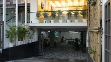 Entrada de un edificio con una marquesina, plantas en macetas y una motocicleta estacionada en el interior.