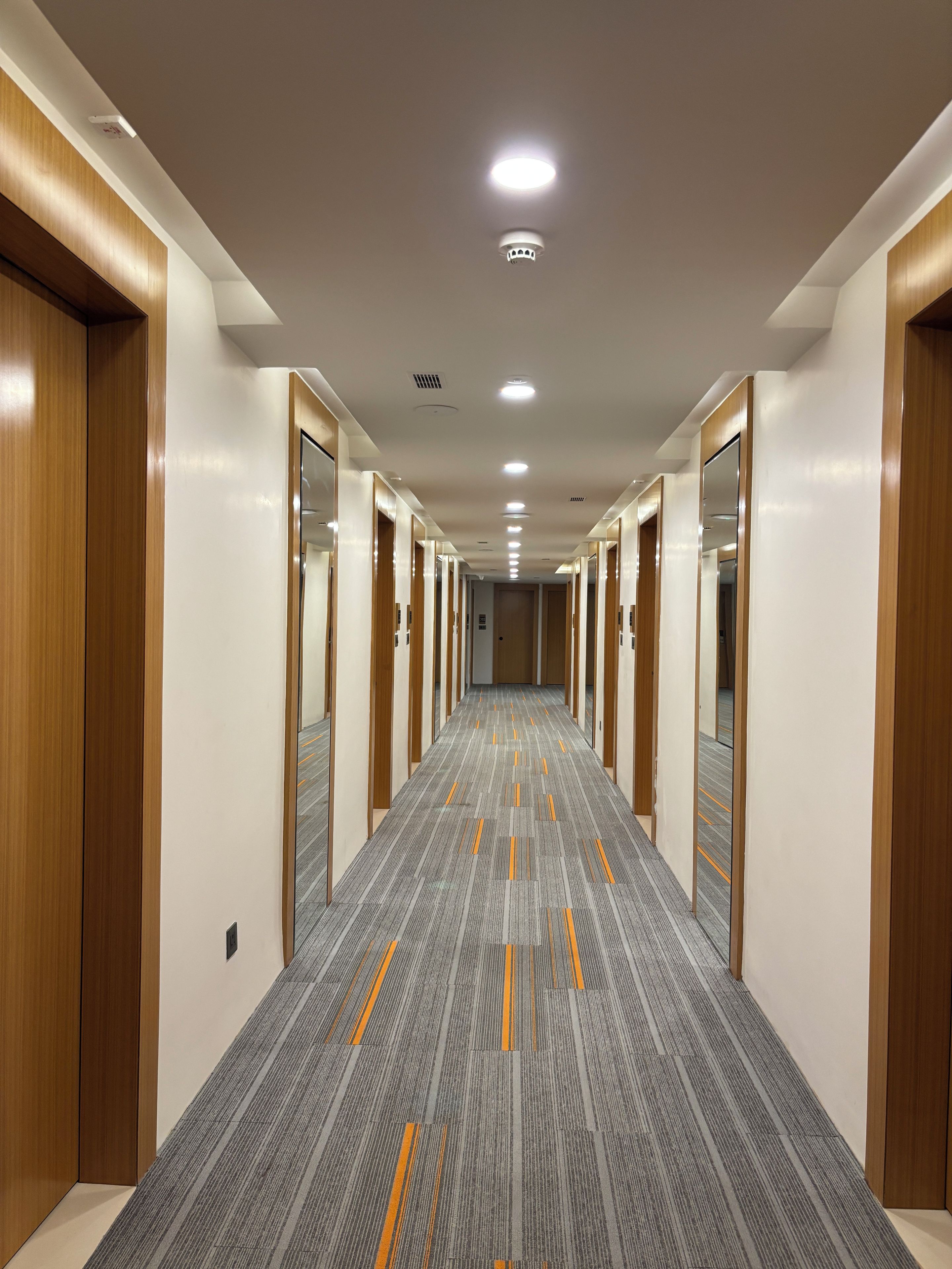 Un couloir d’hôtel avec des portes en bois, des murs recouverts de miroirs et un sol recouvert de moquette.