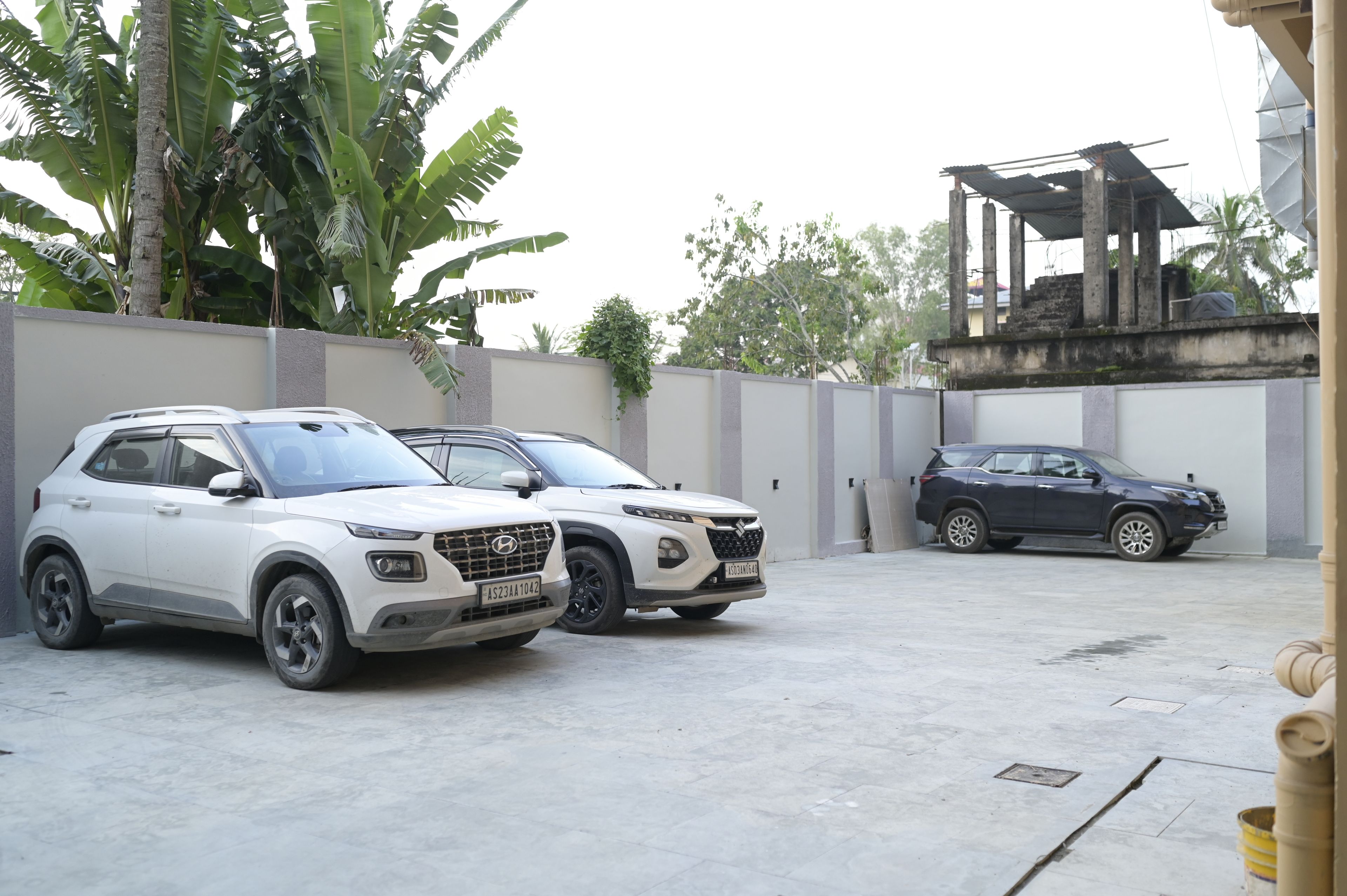 Two parked SUVs in a covered parking area with a concrete floor, surrounded by a low wall and greenery.