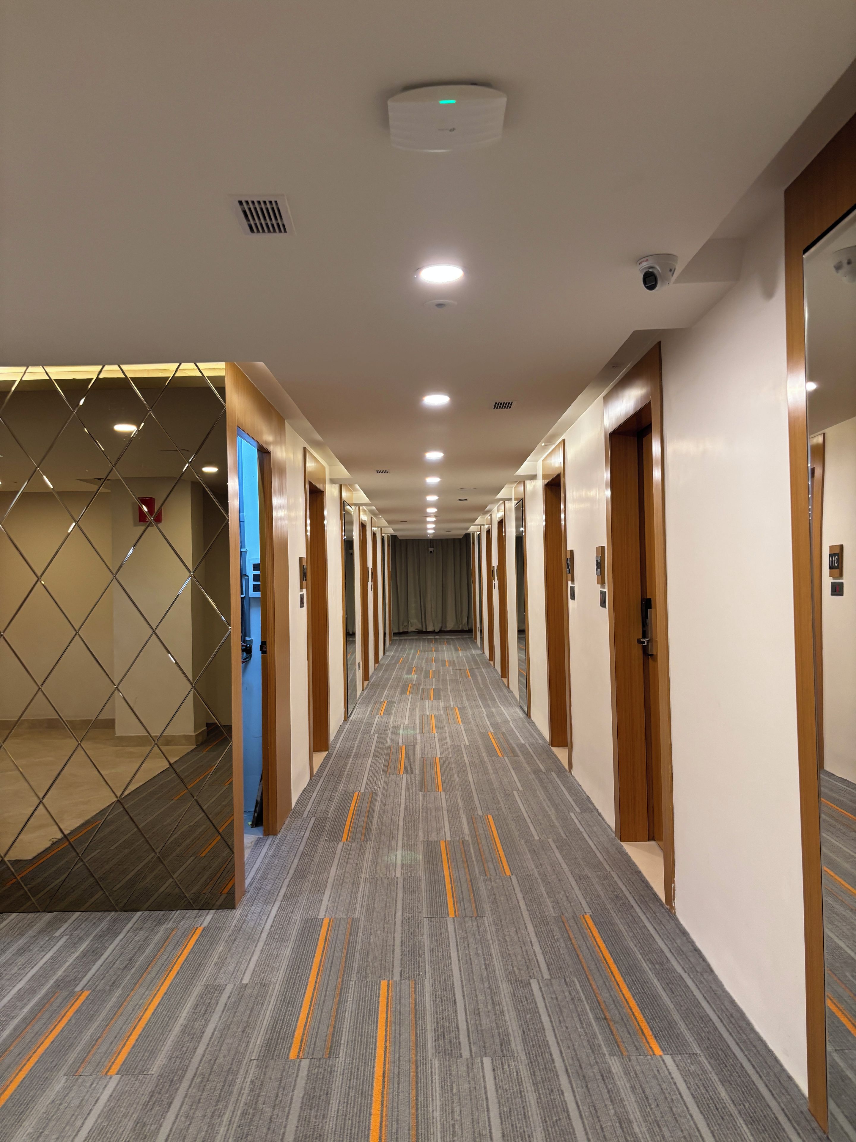A hotel hallway with multiple doors, a patterned carpet, and a ceiling with recessed lighting.