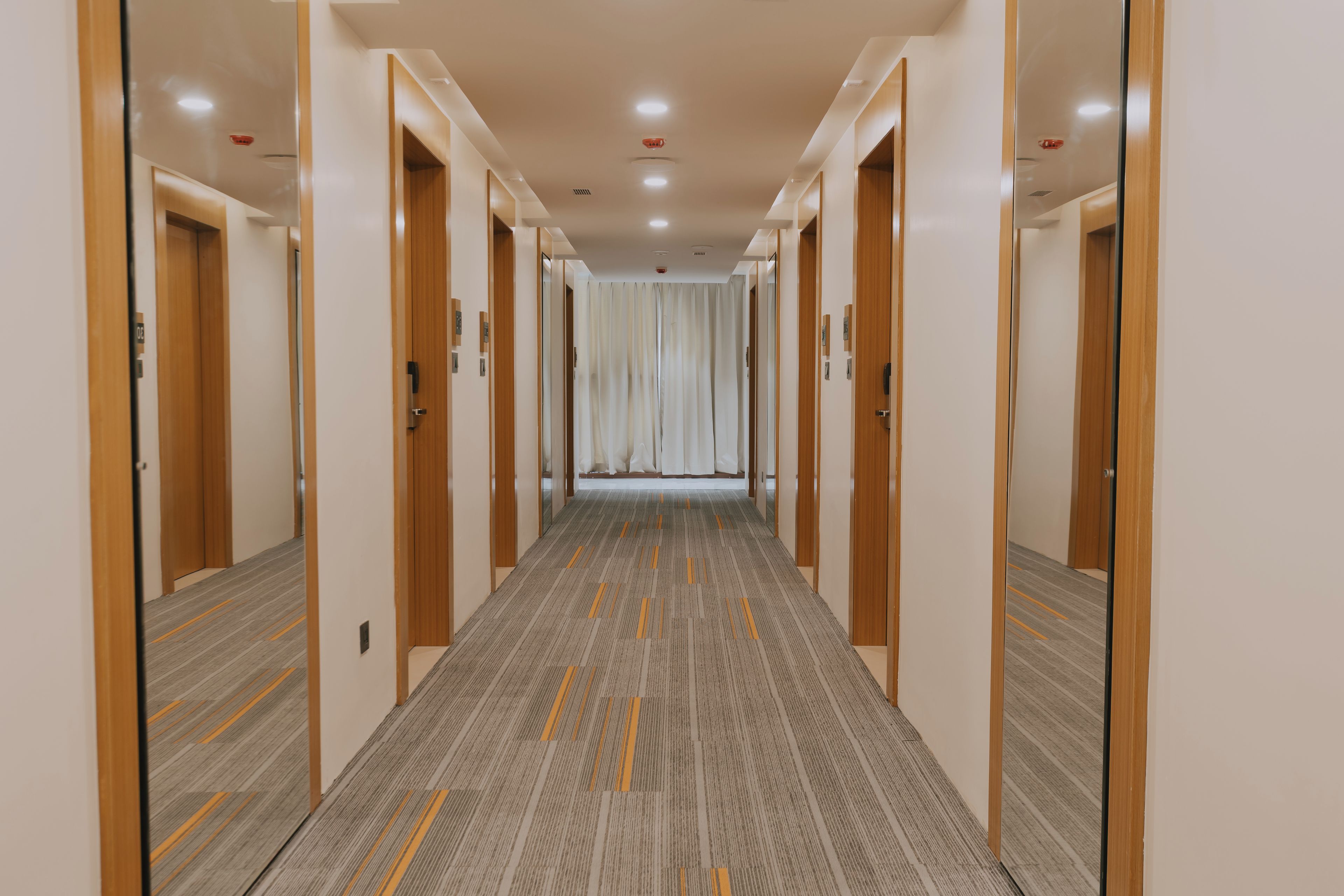 Un pasillo de hotel con paredes espejadas, puertas de madera y suelo alfombrado.