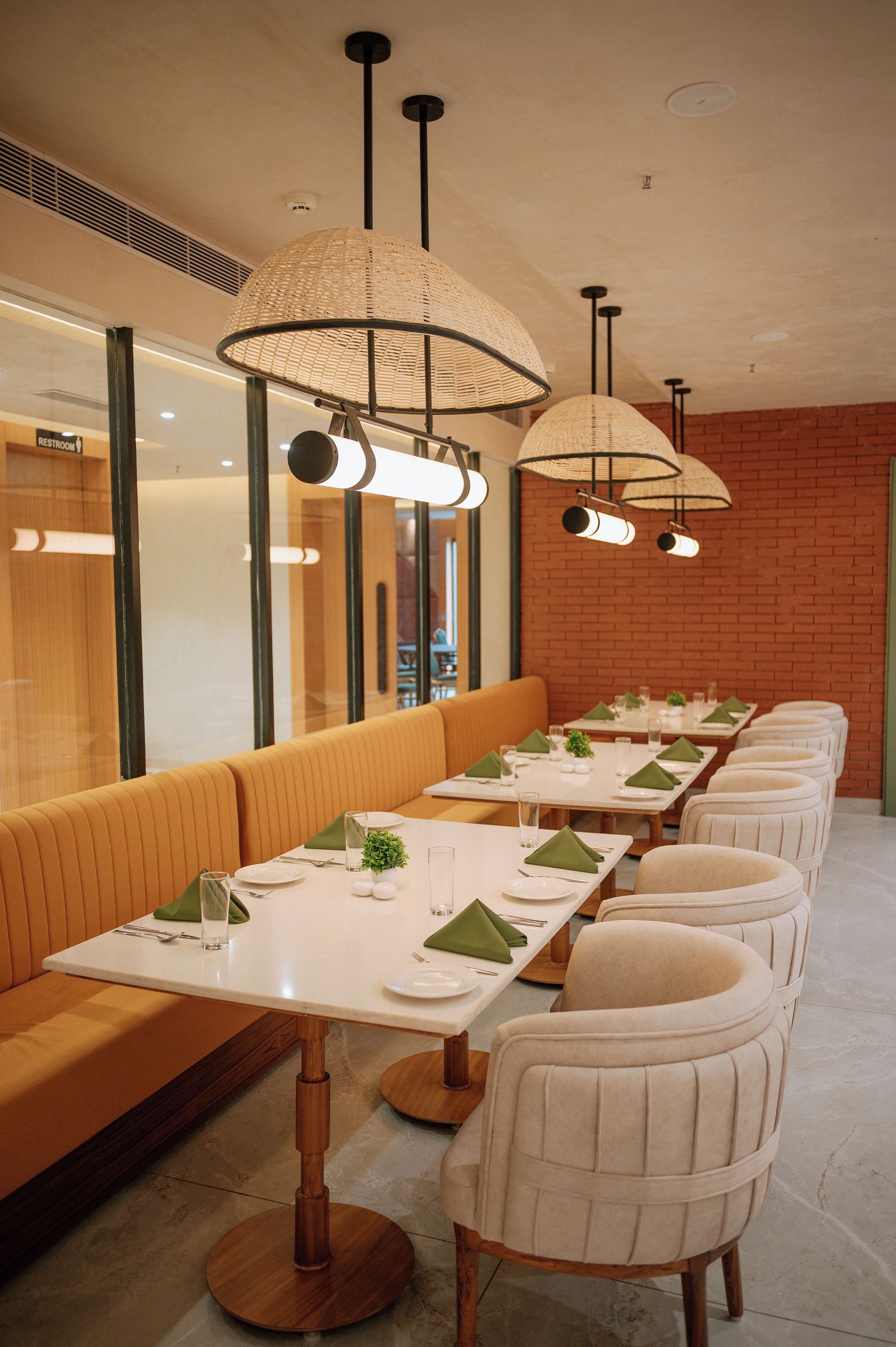 A restaurant interior with long tables, cushioned benches, and pendant lighting.