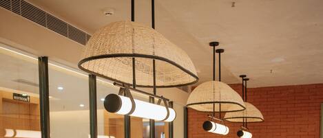 A restaurant interior with long tables, cushioned benches, and pendant lighting.